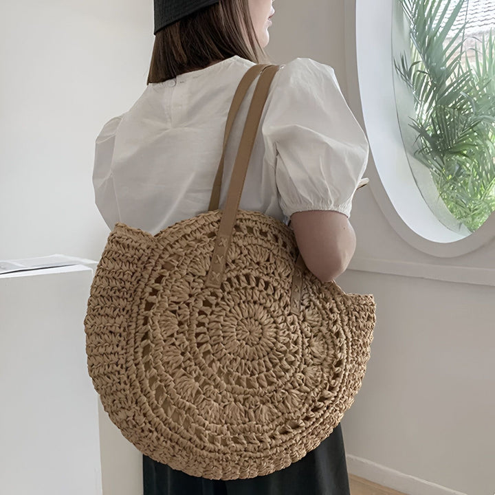 Femme de dos portant un grand sac rond en paille tressée avec anses en cuir., 46194029756640,46194029789408