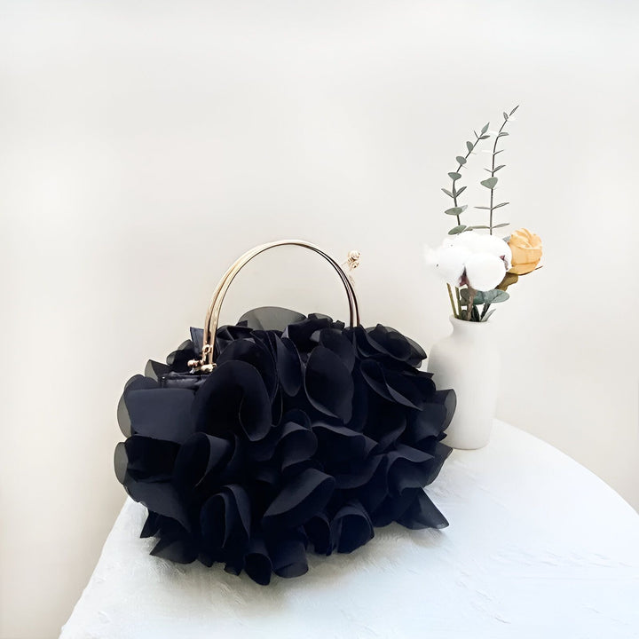 Sac à main noir à volants façon fleur, poignées dorées, sur table blanche., 46193932239072,46193932271840,46193932304608,46193932337376