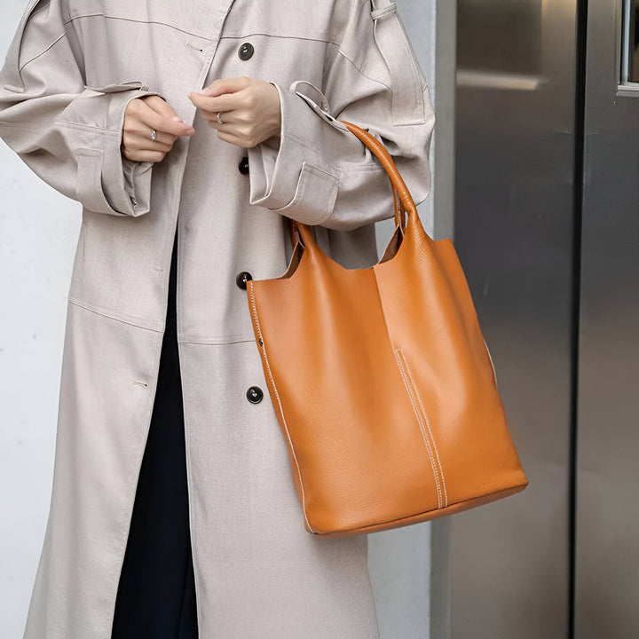 Sac cabas en cuir marron porté par une personne en trench beige., 46193872404704,46193872437472,46193872470240,46193872503008,46193872535776