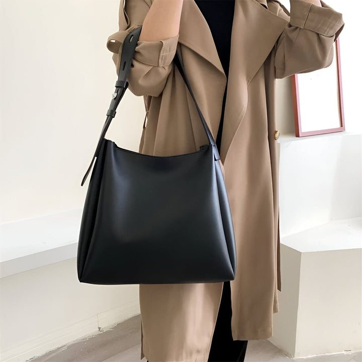 Sac noir porté épaule par une personne en trench coat beige., 46193879515360,46193879548128,46193879580896,46193879613664,46193879646432