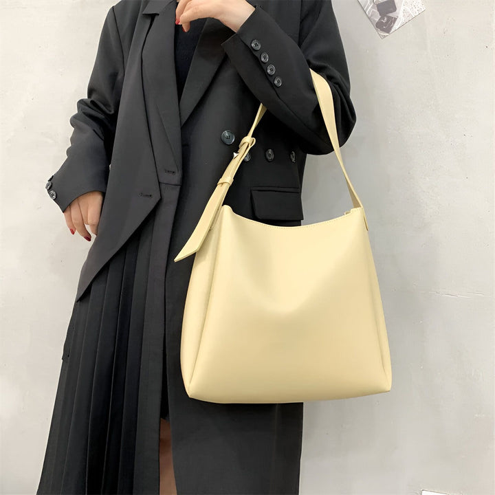 Sac à main jaune pâle porté sur l'épaule avec une tenue noire (blazer et jupe plissée)., 46193879515360,46193879548128,46193879580896,46193879613664,46193879646432