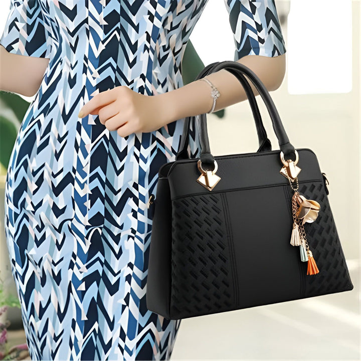 Sac à main noir texturé avec charm, porté par une femme en robe à motif géométrique bleu et blanc., 46193874075872,46193874108640,46193874141408,46193874174176,46193874206944,46193874239712