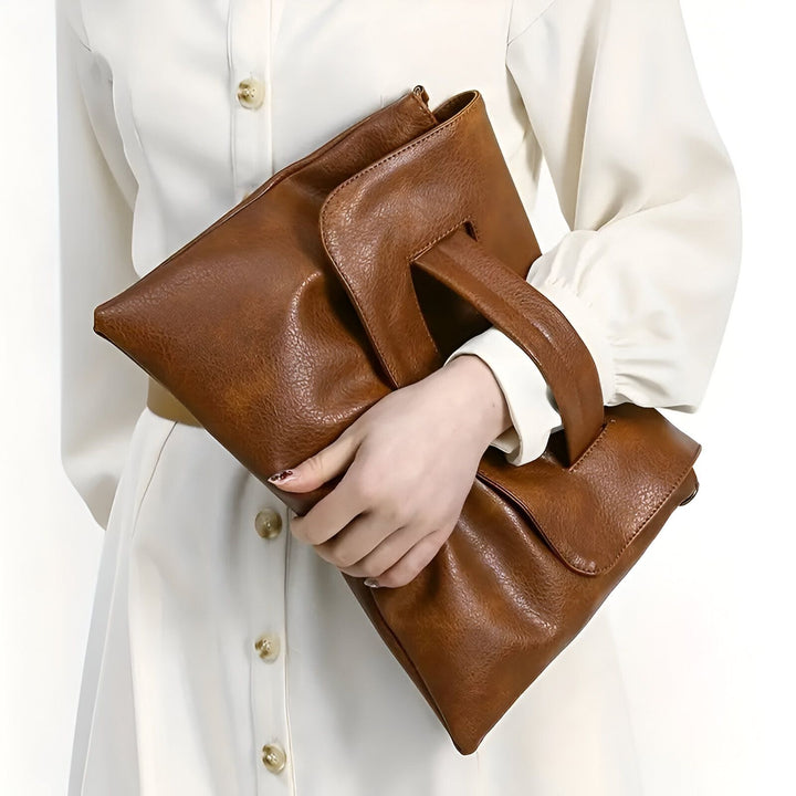 Pochette en cuir marron à poignée tenue par une main., 46194020417760,46194020450528,46194020483296,46194020516064