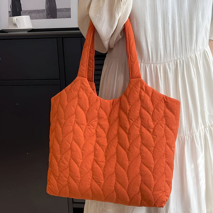 Sac tote orange matelassé avec motif de feuilles, porté par une personne en robe blanche., 46194049712352,46194049745120,46194049777888,46194049810656
