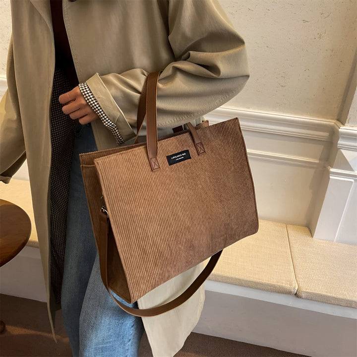 Personne tenant un sac cabas en velours côtelé marron avec anses marron, portant un trench beige., 46194056757472,46194056790240,46194056823008,46194056855776