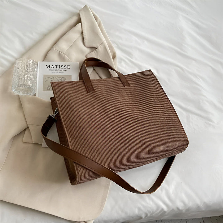 Sac cabas marron en velours côtelé posé sur un lit avec un blazer, un livre Matisse et un verre., 46194056757472,46194056790240,46194056823008,46194056855776
