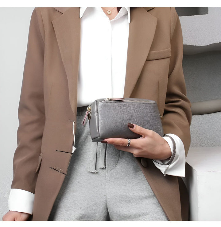 Une femme tenant une pochette en cuir gris. Elle porte un blazer marron et chemise blanche., 46266441924832,46266441957600,46266441990368