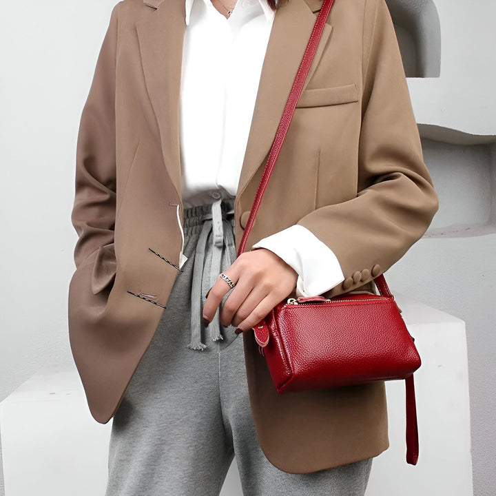 Petit sac bandoulière rouge en cuir texturé tenu par une main portant un anneau., 46266441924832,46266441957600,46266441990368
