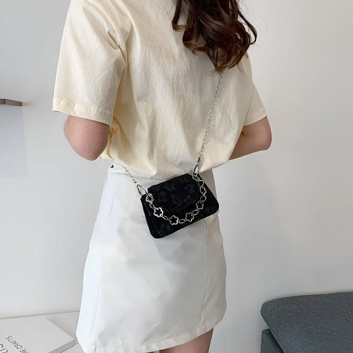 Personne de dos portant un t-shirt jaune pâle et une jupe blanche avec un mini sac noir à chaîne argentée fleurie., 46193968414944,46193968447712,46193968480480,46193968513248,46193968546016