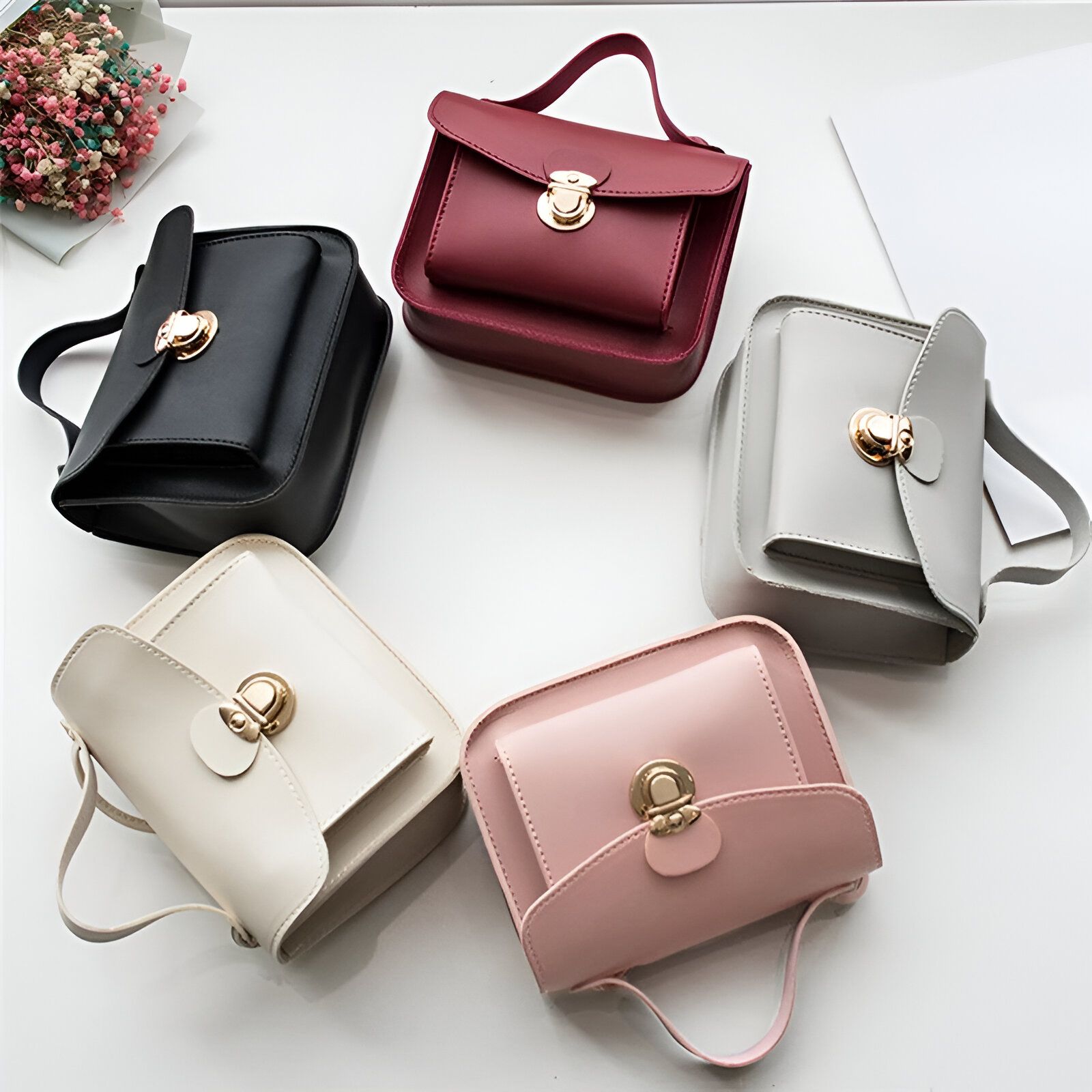 Cinq petits sacs à main en cuir de différentes couleurs : noir, rouge, gris, beige et rose.  Tous les sacs ont une fermeture à boucle dorée.