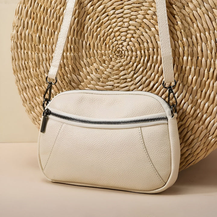 Sac bandoulière blanc crème en cuir texturé avec zip noir, sur fond de paille tressée., 46264208556256,46264208589024