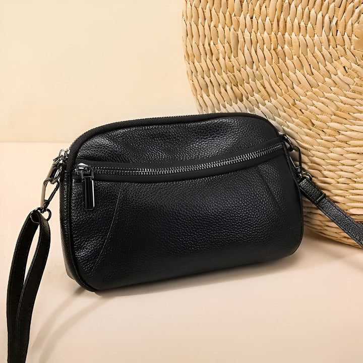 Sacoche noire en cuir grainé avec zips argentés, posée près d'un panier en osier., 46264208556256,46264208589024