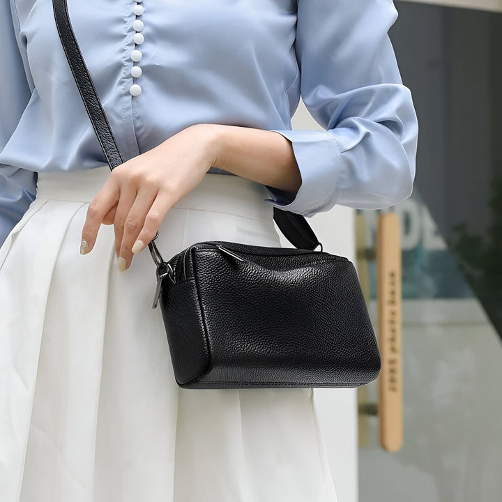 Sac bandoulière en cuir noir porté par une femme en chemise bleue et jupe blanche., 46266441760992,46266441793760