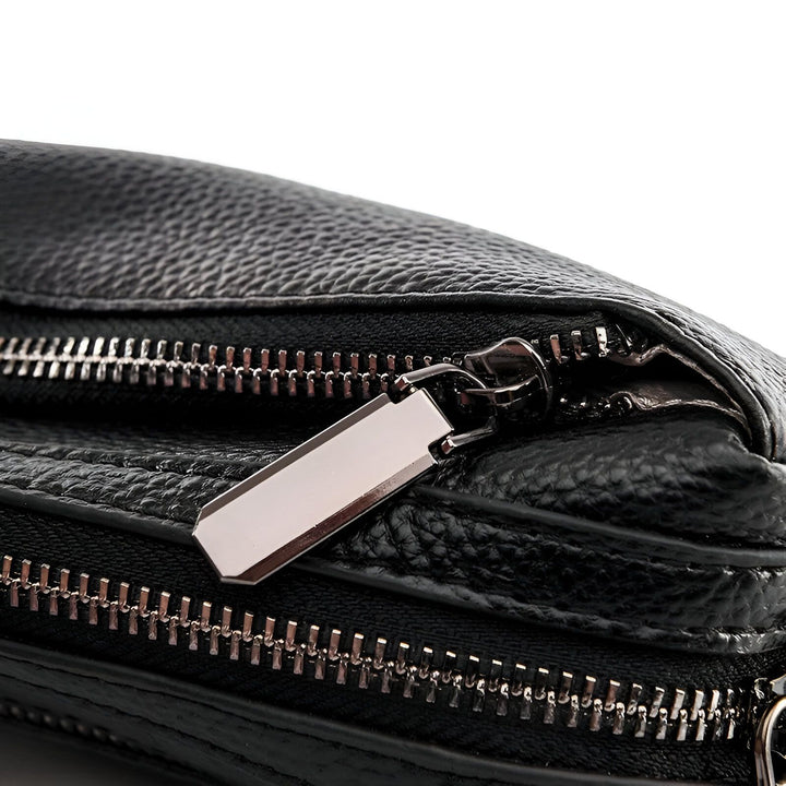 Gros plan sur un zip métallique argenté avec tirette rectangulaire sur un sac en cuir noir texturé., 46266441760992,46266441793760