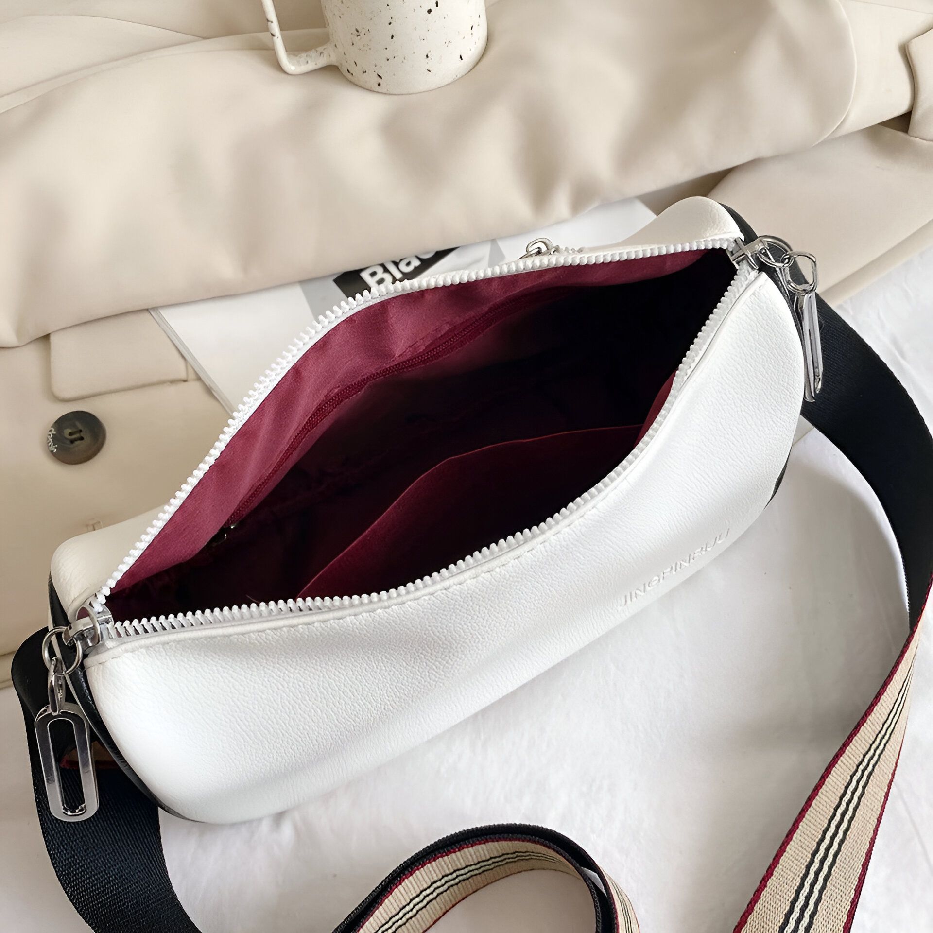 Un sac à bandoulière blanc avec une doublure rouge et une sangle noire et blanche.