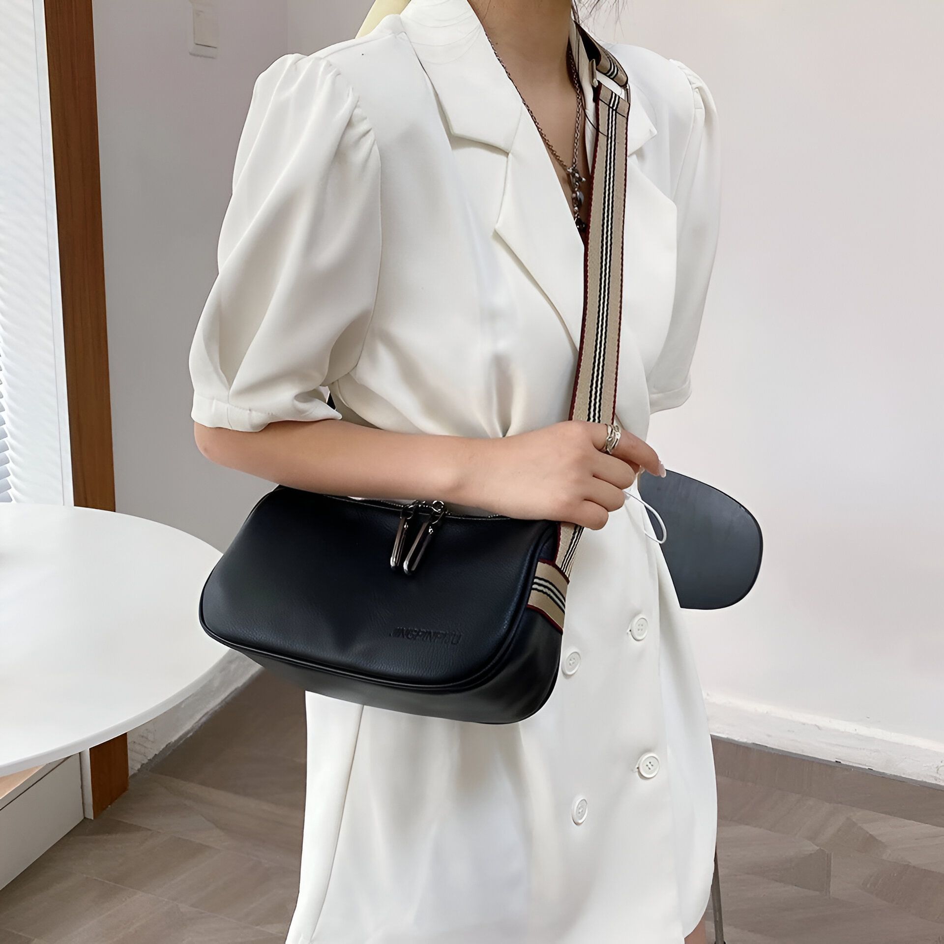 Une femme portant une robe blanche porte un sac à bandoulière noir. Le sac a une longue sangle beige et noire.