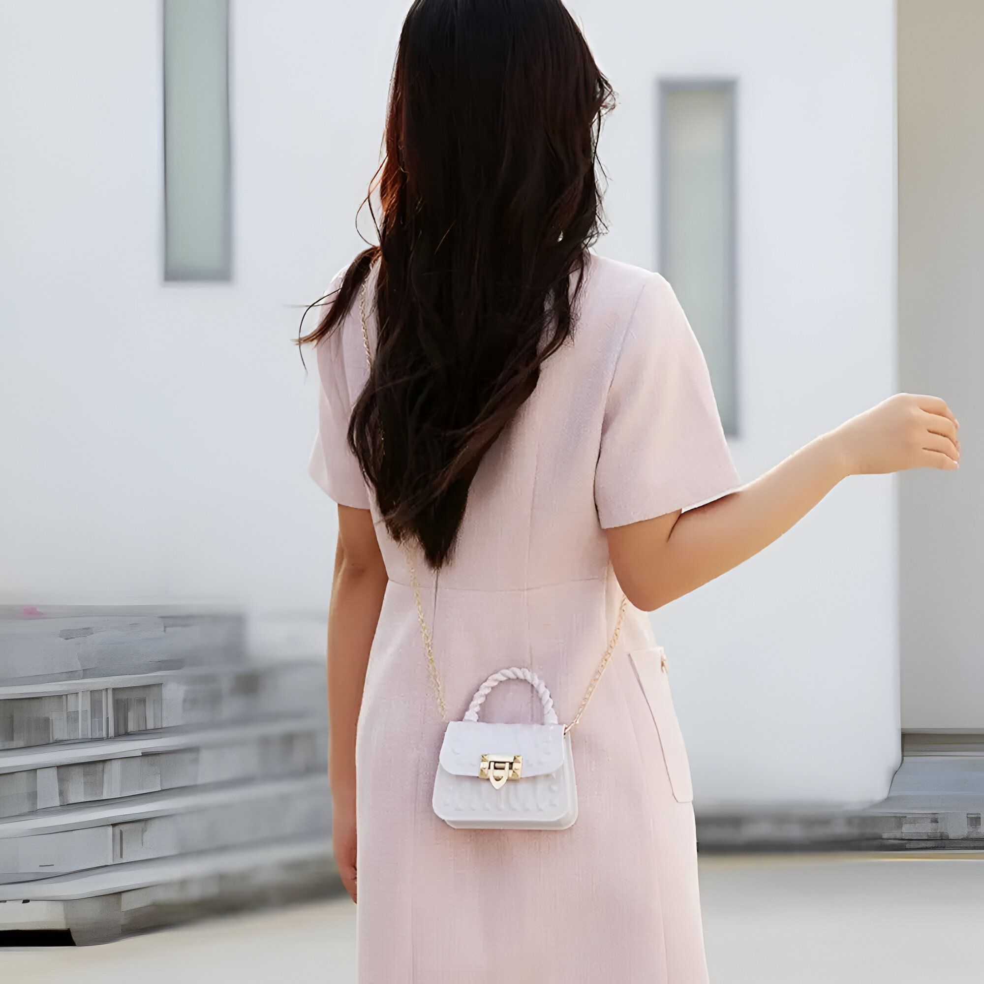 Une femme portant une robe rose et un petit sac à main blanc avec une chaîne en or.