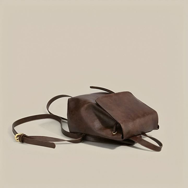 Sac à dos en cuir marron foncé posé sur le côté avec rabat et bandoulière., 46194001805536,46194001838304