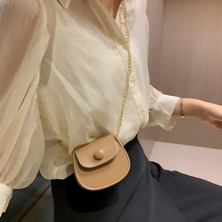 Personne avec mini sac beige à chaîne dorée sur chemisier clair et jupe noire., 46193969856736,46193969889504,46193969922272,46193969955040,46193969987808,46193970020576