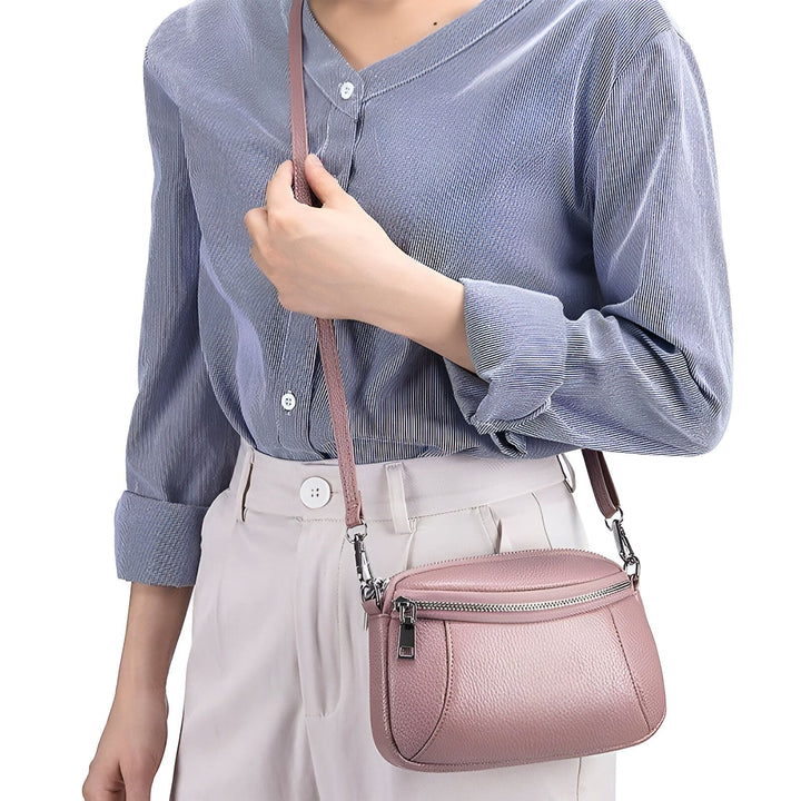 Femme portant un sac bandoulière rose en cuir avec une chemise bleue et un pantalon clair., 46266442121440,46266442154208,46266442186976,46266442219744,46266442252512