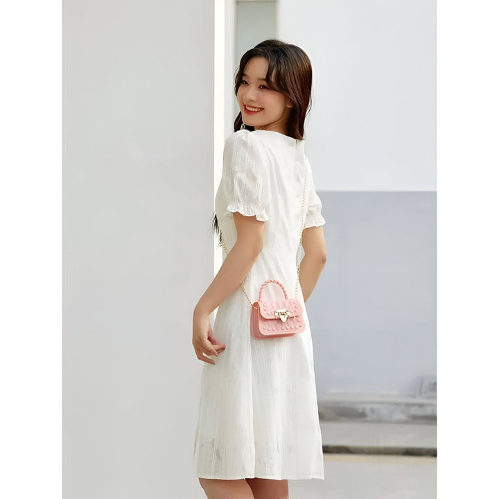 Femme en robe blanche et sac rose regardant par-dessus l'épaule et souriant., 46262992208096,46262992240864,46262992273632,46262992339168,46262992371936,46262992404704,46262992437472