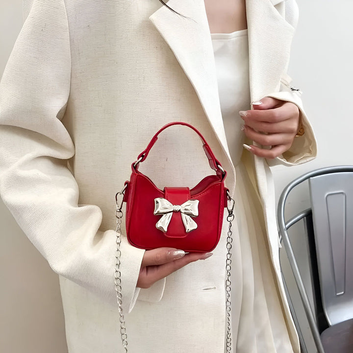Sac à main rouge orné d'un nœud argenté, tenu par une personne portant un blazer blanc., 46262992732384,46262992765152,46262992797920,46262992830688,46262992863456