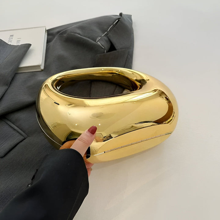 Main tenant une pochette ovale dorée brillante, 46194015502560,46194015535328,46194015568096,46194015600864,46194015633632,46194015666400