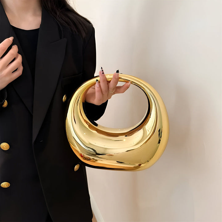 Sac à main rond doré brillant tenu par une personne en blazer noir., 46194015502560,46194015535328,46194015568096,46194015600864,46194015633632,46194015666400