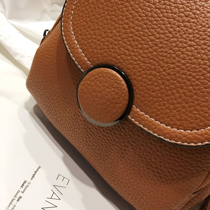 Gros plan sur un sac en cuir marron texturé avec surpiqûres blanches et fermoir circulaire, 46194000822496,46194000855264,46194000888032