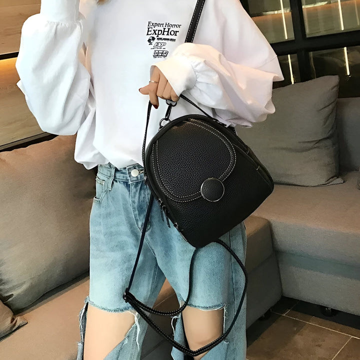 Femme avec chemise blanche et jean déchiré, tenant un petit sac à dos noir en cuir., 46194000822496,46194000855264,46194000888032