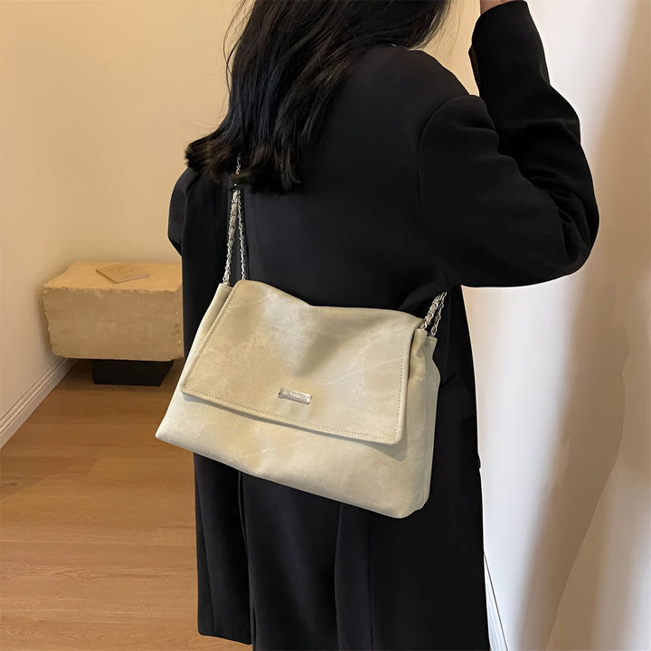 Sac bandoulière beige texturé avec chaîne métallique et rabat, porté sur une veste noire., 46193885544672,46193885577440,46193885610208,46193885642976