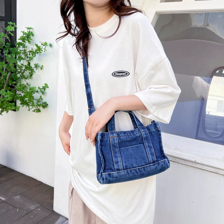 Sac à main en jean bleu porté en bandoulière par une personne., 46193993285856,46193993318624