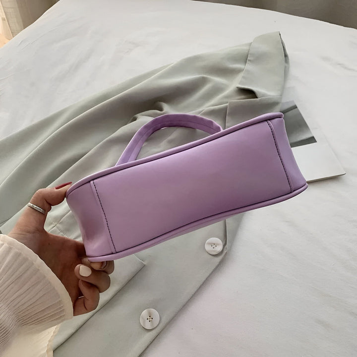 Sac à main violet baguette tenu par une main, posé sur un vêtement gris, 46193965596896,46193965629664,46193965662432,46193965695200,46193965727968,46193965760736,46193965793504