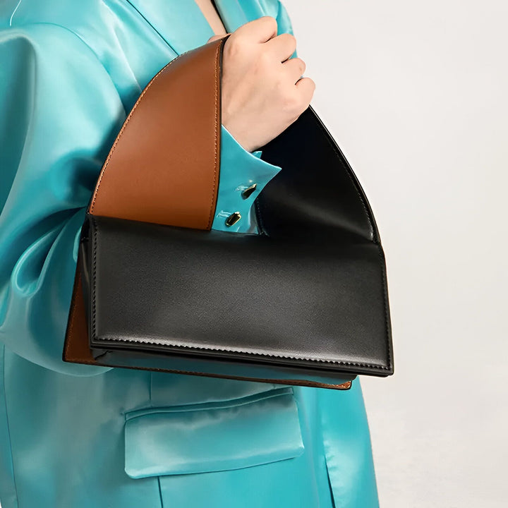 Personne tenant un sac à main en cuir noir et marron, portée avec une veste bleu brillant., 46194016420064