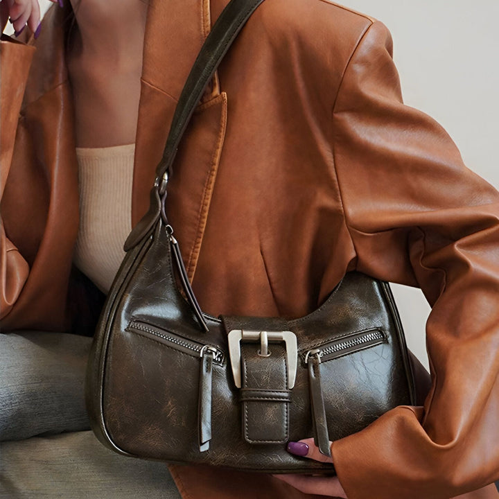 Sac à main baguette marron foncé avec boucle argentée, porté avec une veste en cuir marron., 46193944264928