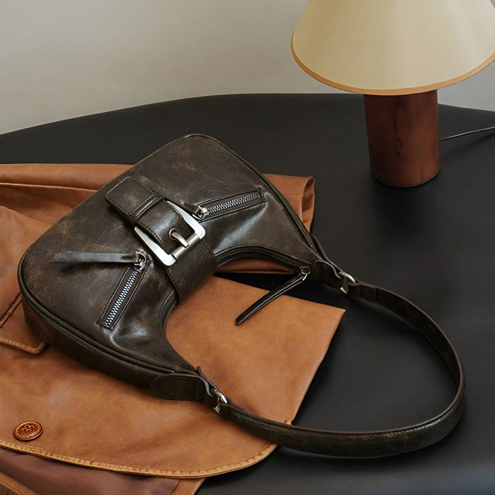 Sac à bandoulière en cuir marron foncé avec fermetures éclair et boucle, posé sur une surface en cuir., 46193944264928