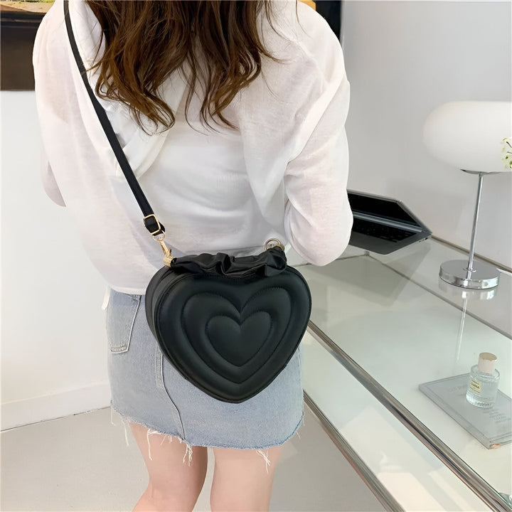Sac bandoulière noir matelassé en forme de cœur porté par une femme., 46193876402400,46193876435168,46193876467936,46193876500704
