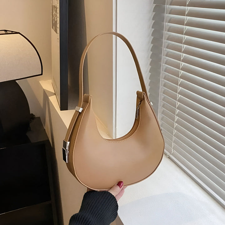 Sac bandoulière forme croissant marron clair tenu par une main., 46193940398304,46193940463840,46193940496608,46193940529376