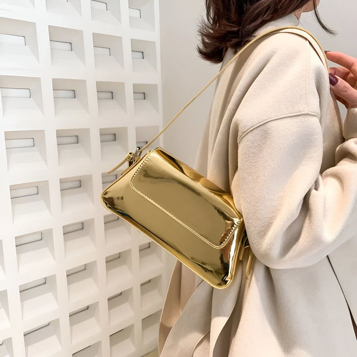 Sac baguette doré brillant porté à l'épaule par une femme en manteau beige., 46194032705760