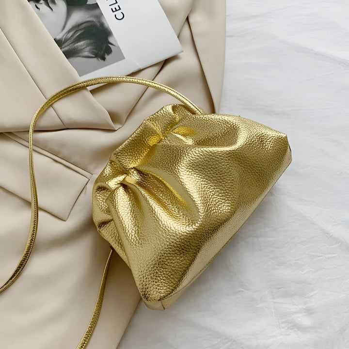Une pochette dorée à texture froissée, avec une fine bandoulière dorée, posée sur un tissu beige., 46194047975648