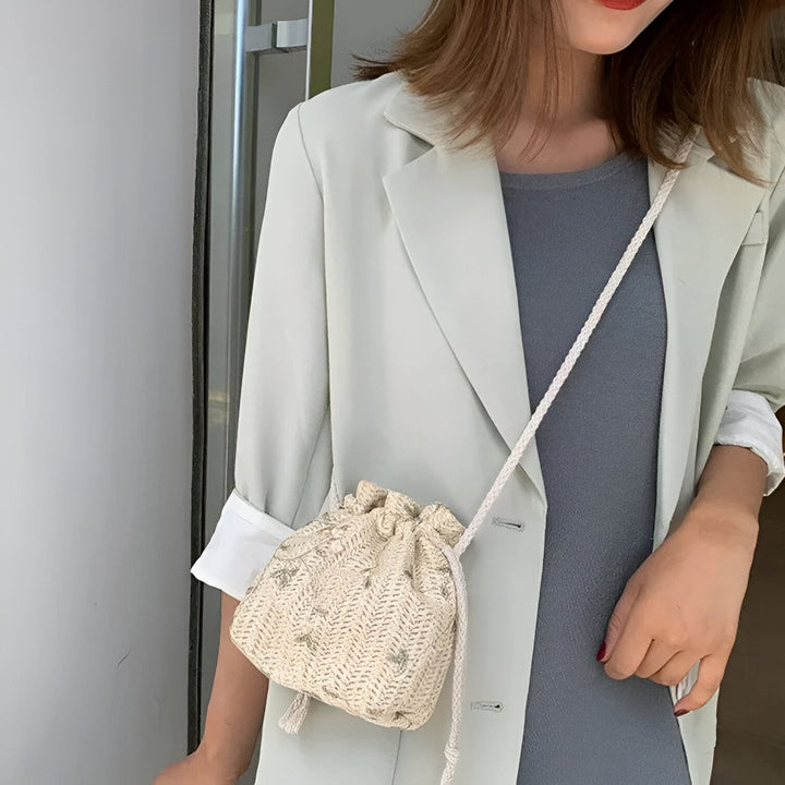 Femme portant un blazer vert pâle et un petit sac bandoulière beige en paille tressée., 46193944494304,46193944527072,46193944559840