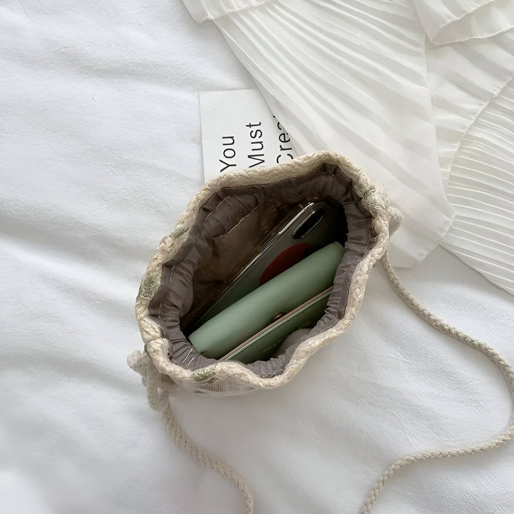Petit sac à cordon beige avec téléphone et portefeuille sur tissu blanc froissé et plissé., 46193944494304,46193944527072,46193944559840