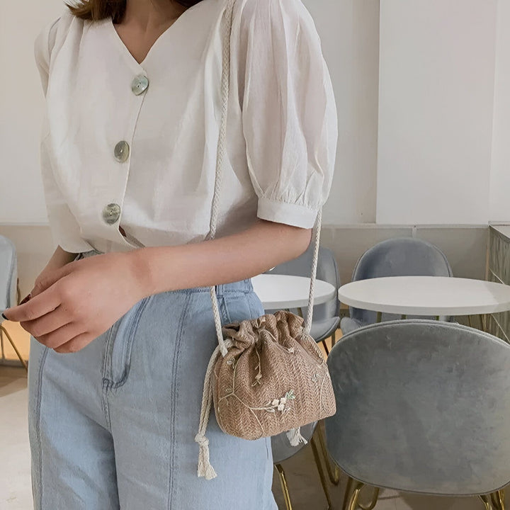 Sac en paille avec fleurs brodées porté par une femme en blouse blanche et jean., 46193944494304,46193944527072,46193944559840