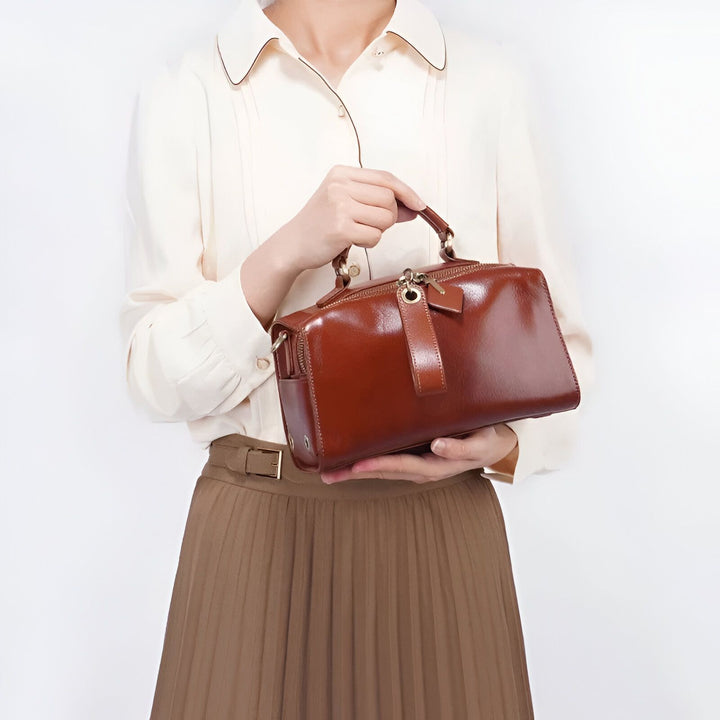 Femme tenant un sac à main en cuir marron brillant, portant une chemise claire et jupe plissée., 46193860182240,46193860215008