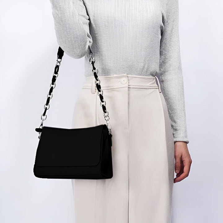 Sac noir à bandoulière chaîne porté par une personne., 46193868505312
