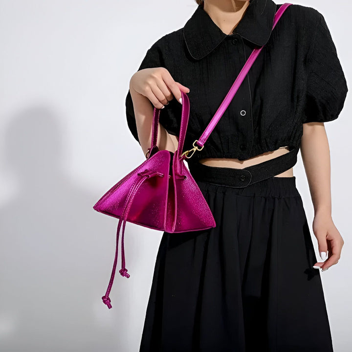 Sac à main rose fuchsia brillant de forme triangulaire porté par une femme en tenue noire., 46194018320608,46194018353376,46194018386144,46194018418912,46194018451680,46194018484448