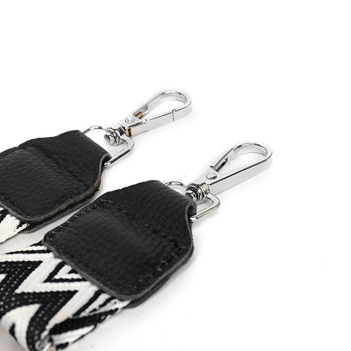 Deux mousquetons chromés attachés à une sangle motif zigzag noir et blanc avec pattes en cuir noir., 46194065080544,46194065113312,46194065146080,46194065211616,46194065244384