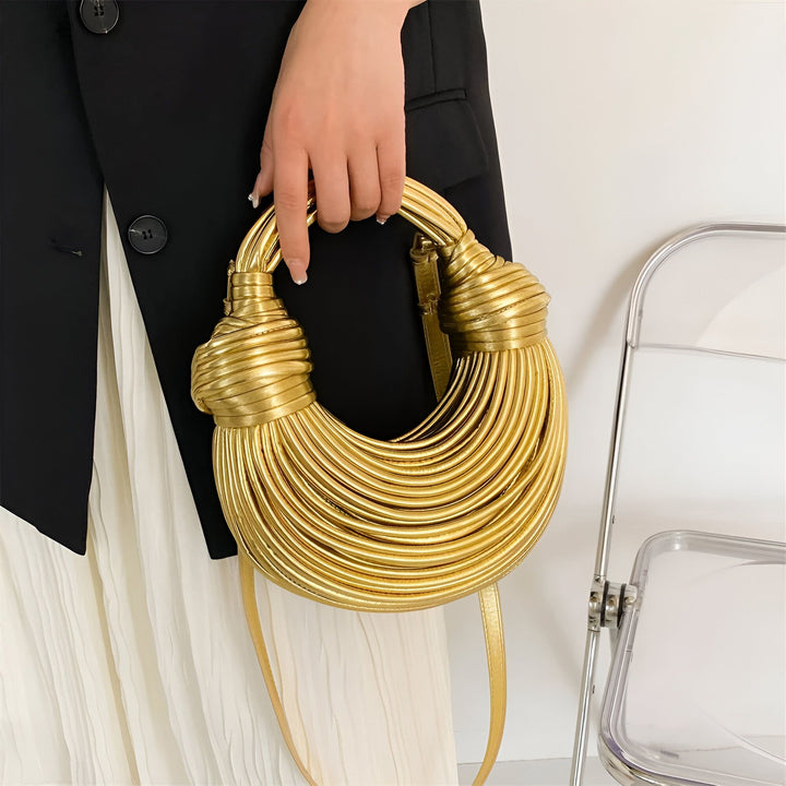 Sac à main doré texturé en forme de croissant tenu par une main., 46194034737376