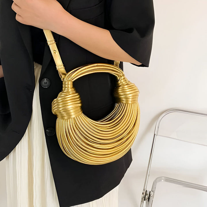 Sac à main doré texturé avec nervures et nœuds, porté par une personne., 46194034737376