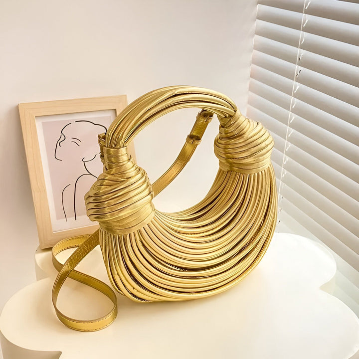 Sac à main clutch doré avec anse et corps plissés, sur une table blanche., 46194034737376